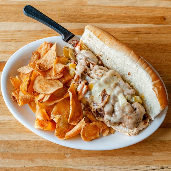 A Vivio's II cheesesteak sandwich with melted cheese, onions, and peppers, served with crispy chips.