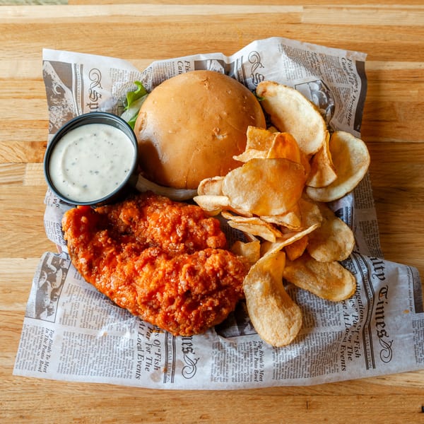 Vivio's II Food & Spirits' spicy chicken sandwich with chips and ranch dressing on newspaper.