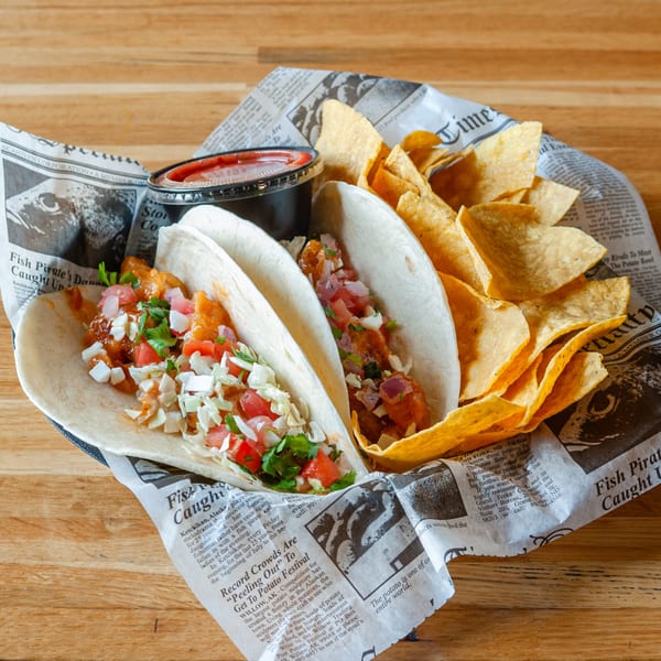 Two Vivio's II fish tacos with salsa and tortilla chips, served on newspaper-print paper.