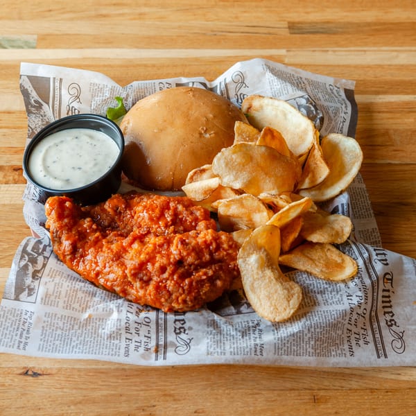 Vivio's II Food & Spirits' buffalo chicken sandwich with chips and ranch dressing on newspaper.
