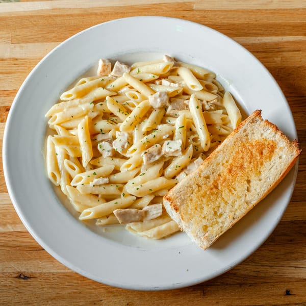 Creamy penne pasta with chicken and parsley, served with a slice of toasted garlic bread.