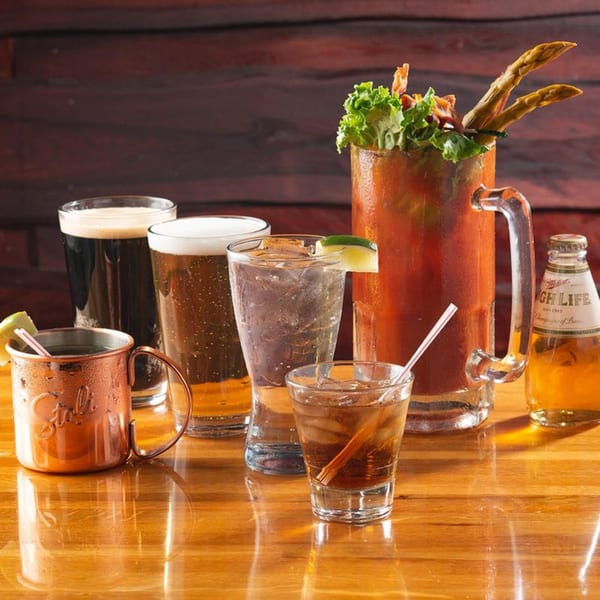 Assortment of drinks, including beers, a Moscow Mule, and a Bloody Mary, on a wooden table.