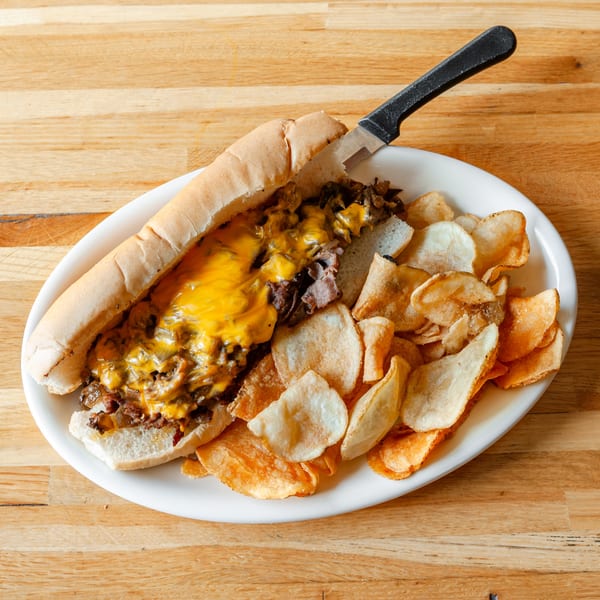Vivio's II Food & Spirits' cheesesteak sandwich with melted cheese and chips on a white plate.